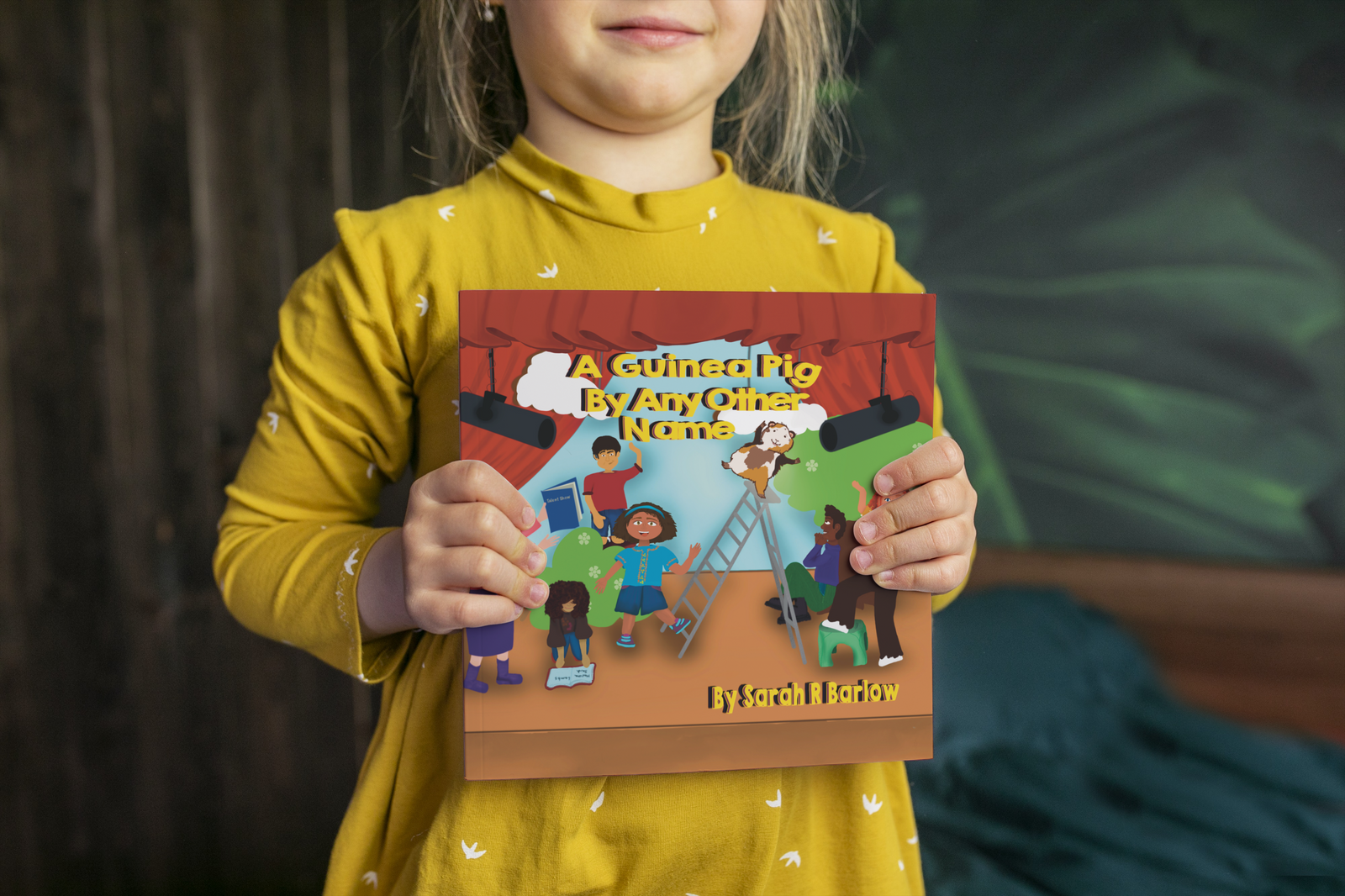 a child holding up the children's book, A Guinea Pig by Any Other Name, by Sarah R Barlow. 